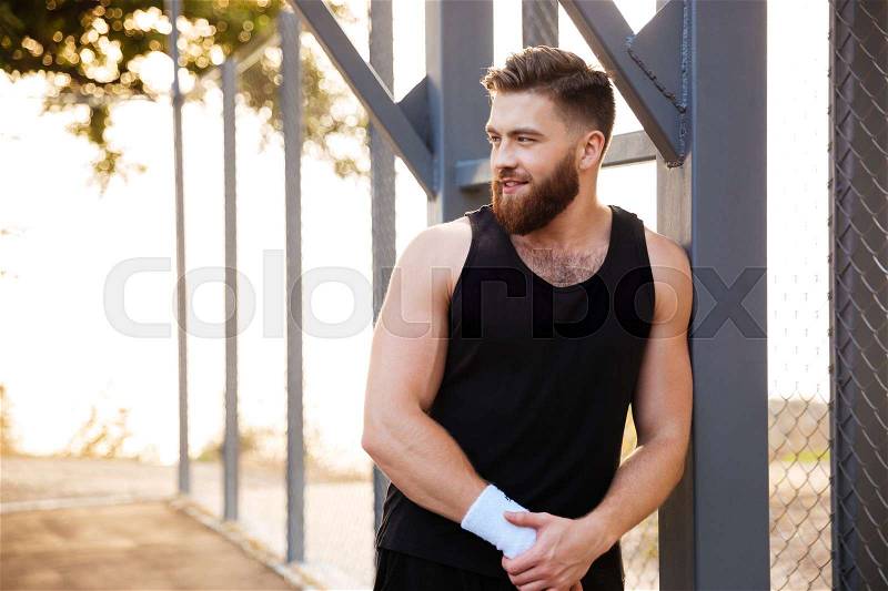 Smiling bearded young athlete standing outdoors and looking away, stock photo