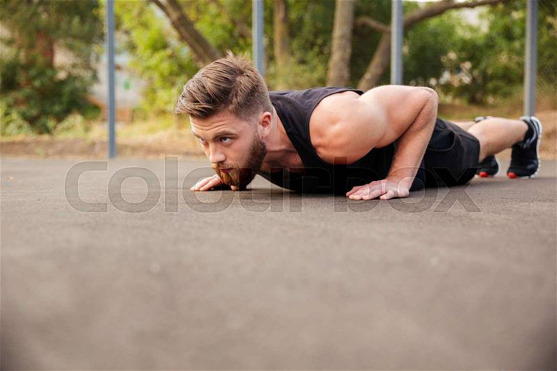 Handsome bearded young sportsman doing push-ups outdoors, stock photo