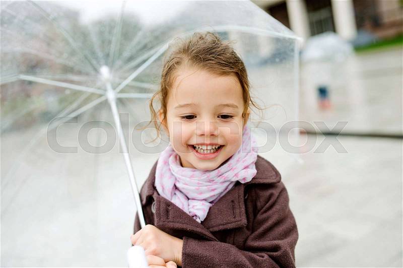 Cute little girl under the transparent umbrella in town on a rainy day, stock photo