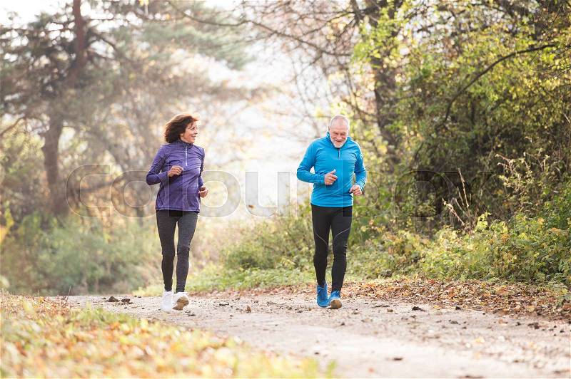 Beautiful active senior couple running together outside in sunny autumn forest, stock photo