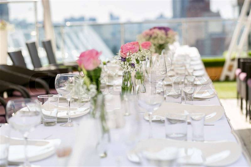 Row of vases with flowers on long table served for wedding banquet on restaurant summer terrace, stock photo