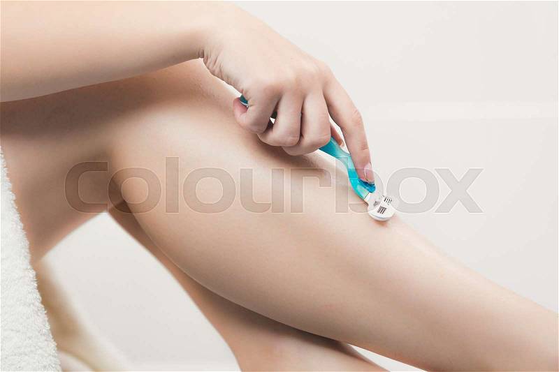 Closeup toned image of young woman holding razor and shaving legs at bathroom, stock photo