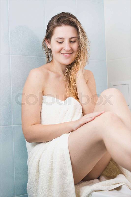 Portrait of beautiful young woman covered in white bath towel sitting at bathroom, stock photo
