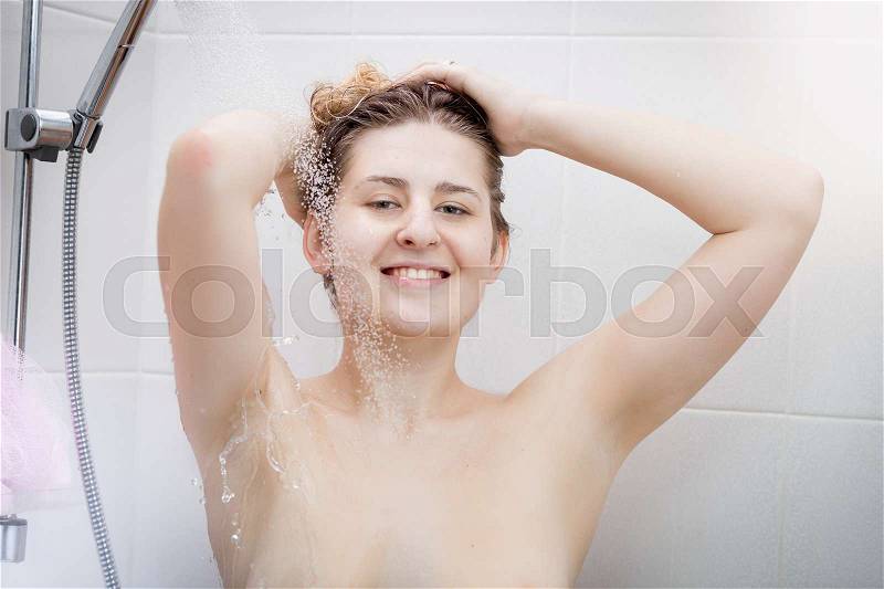 Closeup portrait of young positive woman washing hair with shampoo at shower, stock photo