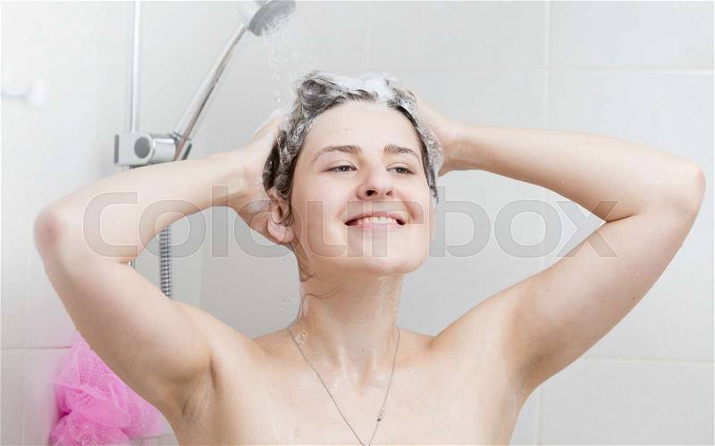 Portrait of beautiful smiling woman washing hair in shower stall, stock photo
