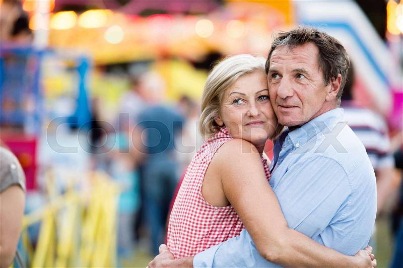 Senior couple having a good time at the fun fair, hugging. Sunny summer day, stock photo