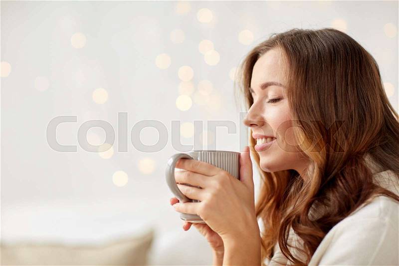 Morning, leisure, christmas, winter and people concept - happy young woman with cup of coffee or tea at home, stock photo