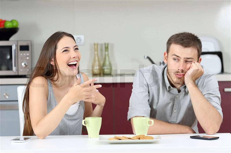 Bored husband hearing his wife talking during breakfast in the kitchen at home, stock photo