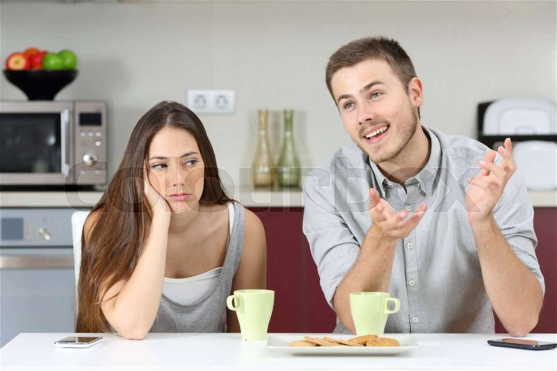 Bored wife hearing her husband talking during breakfast in the kitchen at home, stock photo
