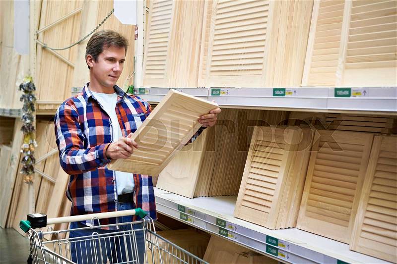 Man chooses wooden facades for furniture in store construction materials, stock photo