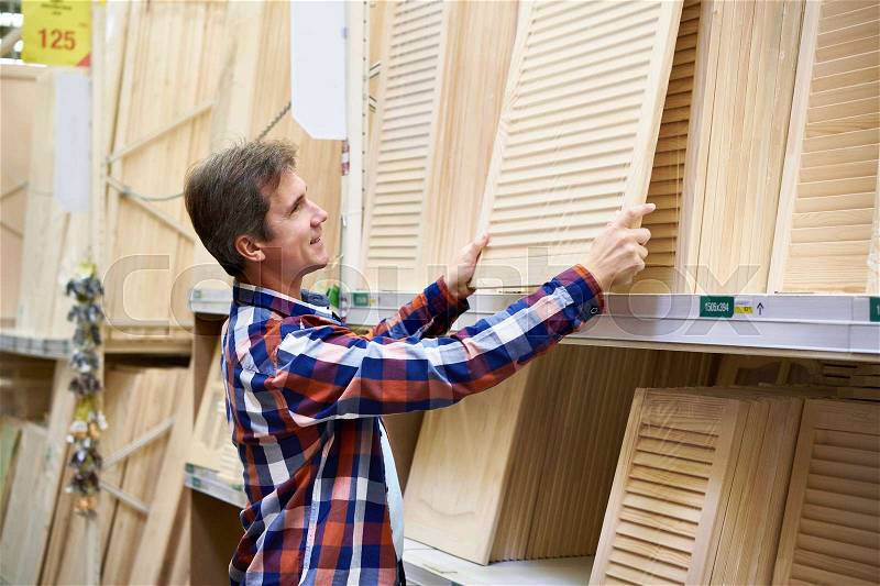 Man chooses wooden facades for furniture in store construction materials, stock photo