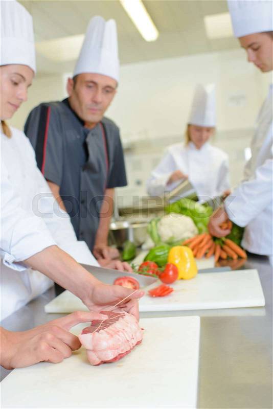 Chef watching student tie joint of meat, stock photo