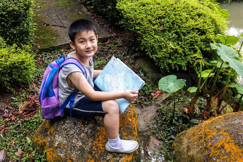 Smiling Asian Chinese little boy holding map sitting in the forest, stock photo