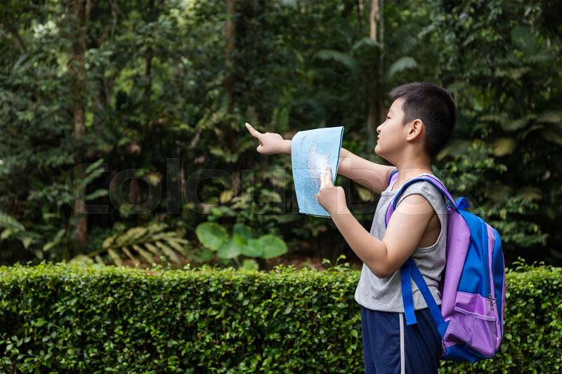 Asian Chinese little boy holding map pointing in the forest looking for direction, stock photo