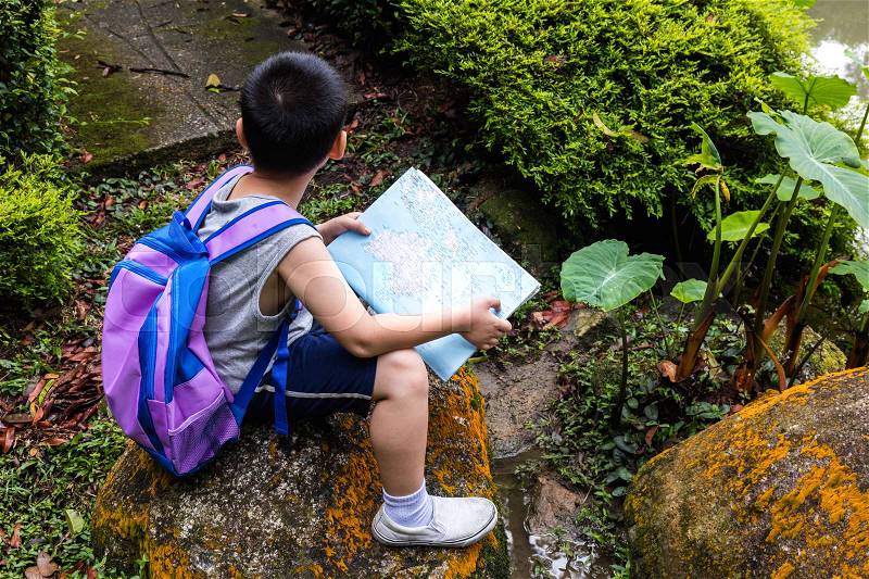 Asian Chinese little boy holding map sitting on the rock in the forest, stock photo