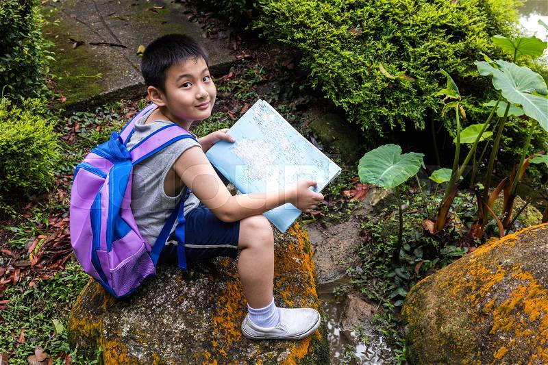 Smiling Asian Chinese little boy holding map sitting in the forest, stock photo