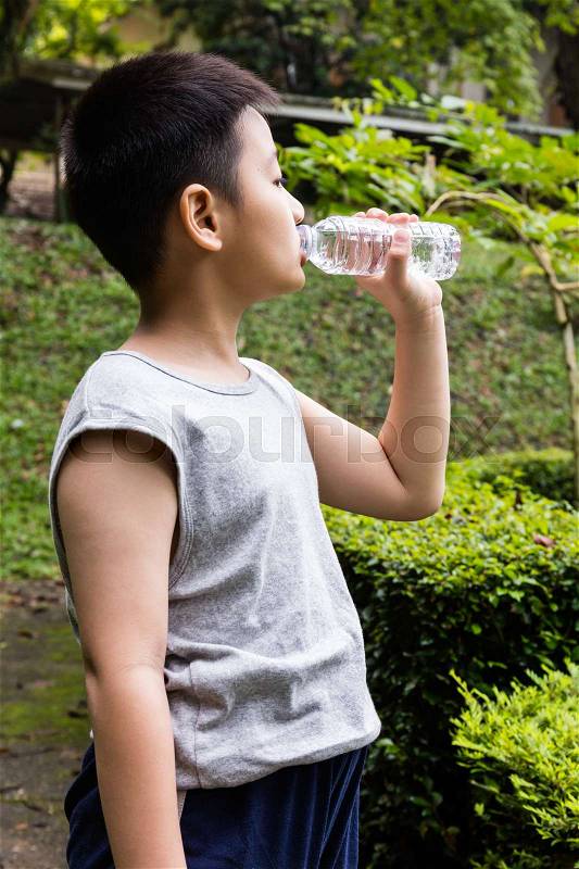 Asian Chinese little boy drinking mineral water at outdoor park, stock photo