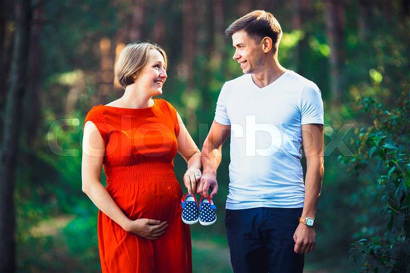 Pregnant wife and her husband holding a small baby shoes and pose for the camera, stock photo
