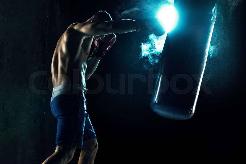 Male Athlete boxer punching a punching bag with dramatic edgy lighting in a dark studio, stock photo