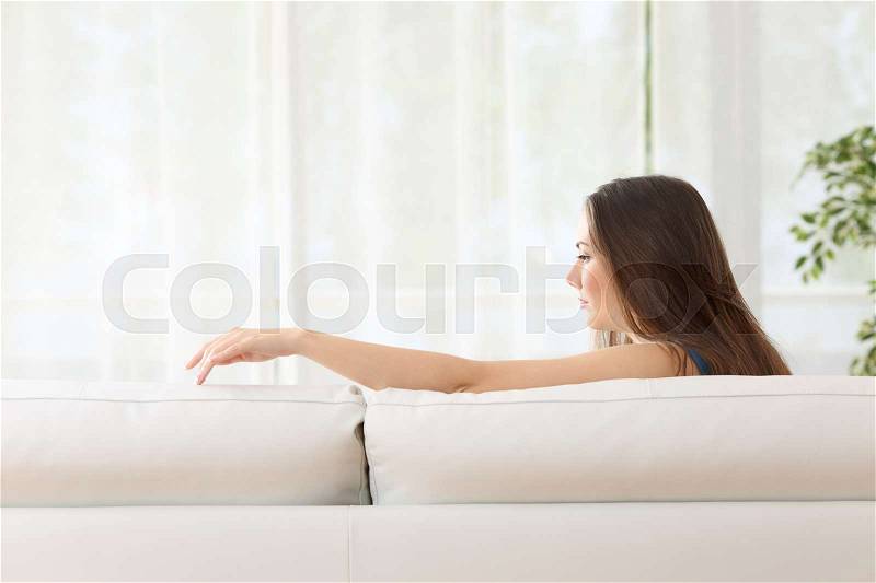Sad woman sitting on a couch missing her lost husband touching the empty seat at home, stock photo
