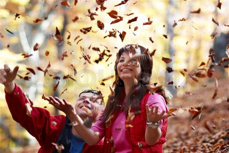 Young couple enjoying the falling leaves in the autumn park, stock photo