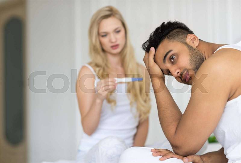 Young Couple Sitting In Bed, Woman Show Man Positive Pregnancy Test Conflict Relationships Problem, Sad Negative Emotions Lovers Bedroom, stock photo