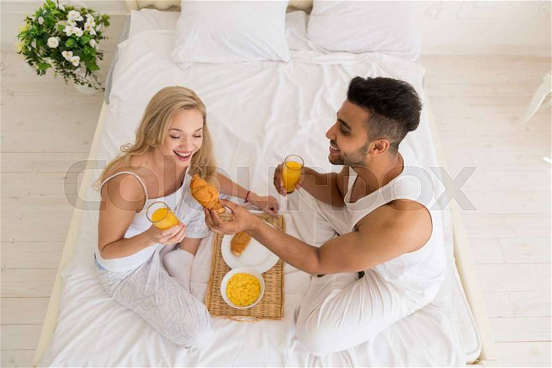 Young Couple Breakfast Sitting In Bed, Happy Smile Young Hispanic Man And Woman Morning Top Angle View Lovers Bedroom, stock photo
