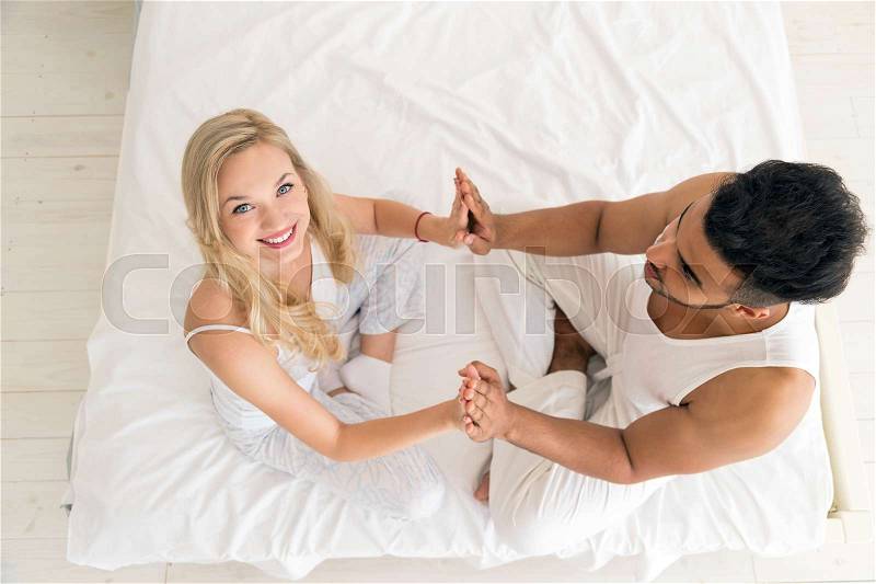 Young Couple Hold Hands Sitting In Bed, Happy Smile Young Hispanic Man And Woman Top Angle View Lovers Bedroom, stock photo