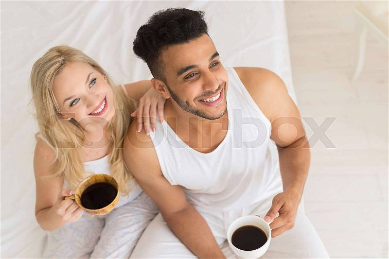 Young Couple Drink Coffee Sitting In Bed, Happy Smile Young Hispanic Man And Woman Top Angle View Lovers Hold Cups Bedroom, stock photo