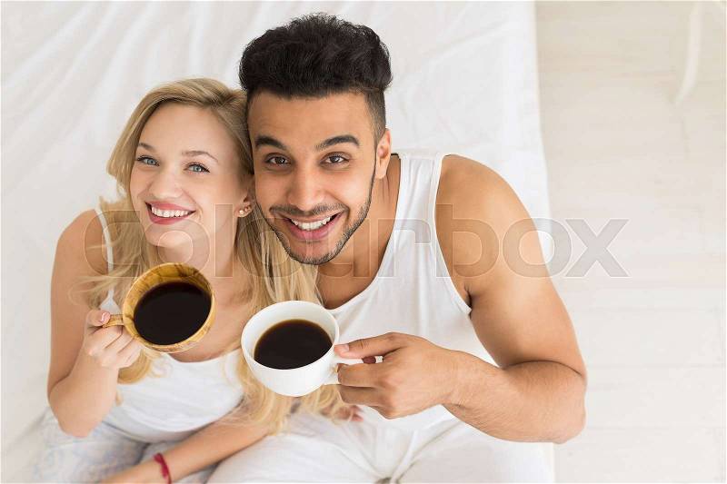 Young Couple Drink Coffee Sitting In Bed, Happy Smile Young Hispanic Man And Woman Top Angle View Lovers Hold Cups Bedroom, stock photo