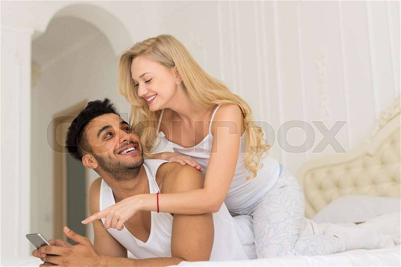 Young Couple Lying In Bed, Happy Smile Hispanic Man And Woman Using Cell Smart Phone, Lovers In Bedroom, stock photo