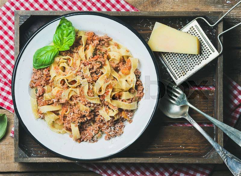Italian pasta dinner. Homemade Tagliatelle Bolognese with Parmesan cheese and fresh basil in wooden tray over rustic wooden background, top view, stock photo