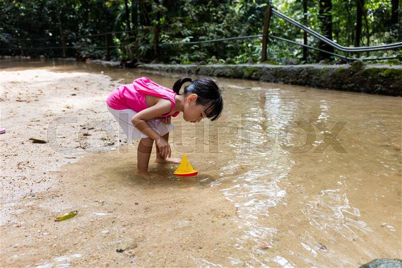 Asian Chinese little girl playing toy boat at creek in bare foot, stock photo