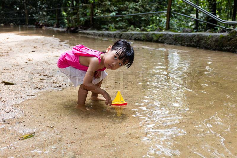 Asian Chinese little girl playing toy boat at creek in bare foot, stock photo