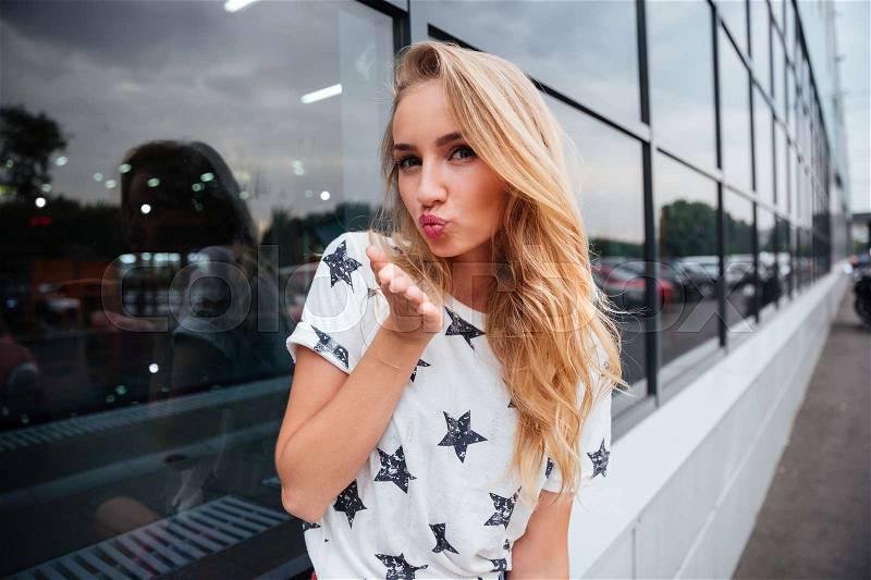 Beautiful young woman sending air kiss while standing outdoors, stock photo