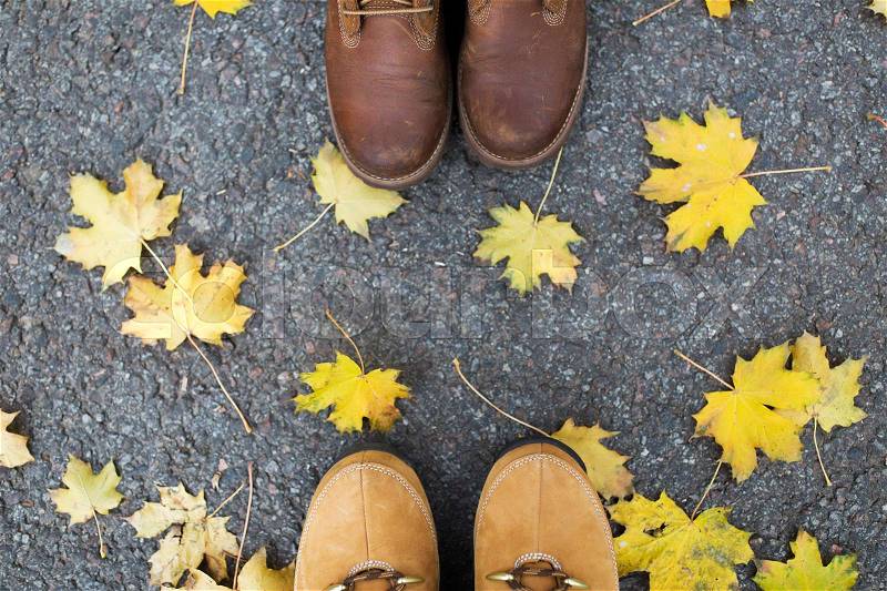 Season and people concept - couple of feet in boots with autumn leaves on ground, stock photo