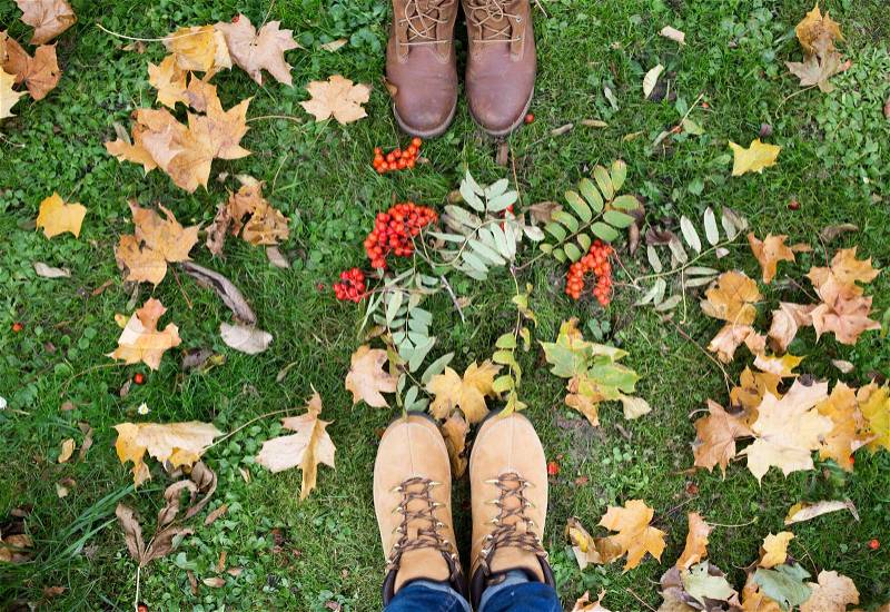 Season and people concept - couple of feet in boots with rowanberries and autumn leaves on grass, stock photo