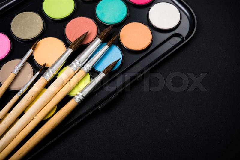 New watercolor paint set and brushes on artist\'s work desk, creative art tools isolated on black background closeup, stock photo