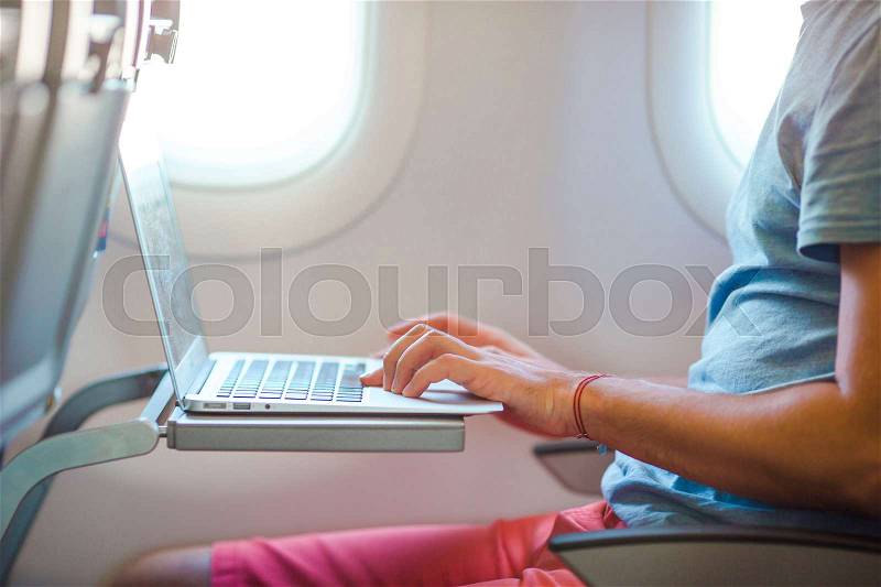 Young man sitting in the airplane and working on his laptop, stock photo
