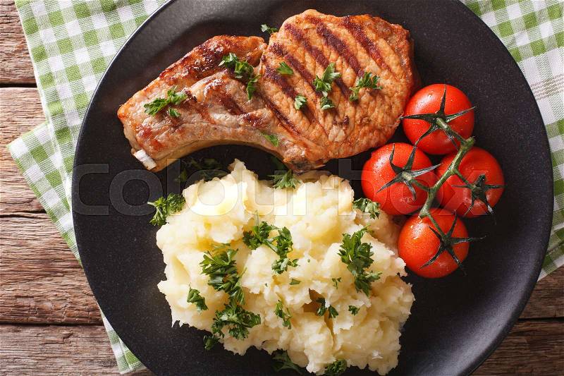 Grilled pork T-bone steak garnished with mashed potatoes and tomato close-up on a plate. Horizontal view from above , stock photo