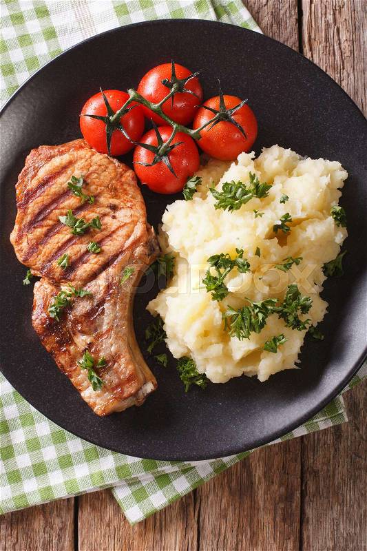 Grilled pork T-bone steak garnished with mashed potatoes and tomato close-up on a plate. vertical view from above\, stock photo