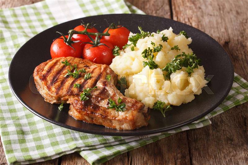 Grilled pork T-bone steak garnished with mashed potatoes and tomato close-up on a plate. horizontal , stock photo