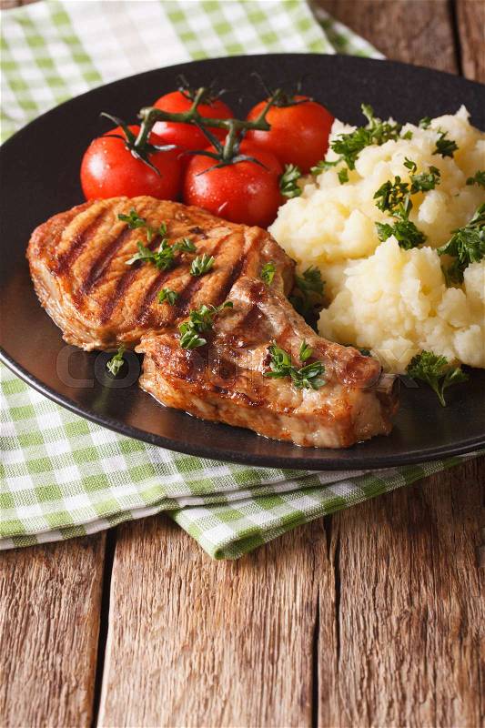 Grilled pork loin with mashed potatoes and tomato close-up on a plate. Vertical, rustic\, stock photo