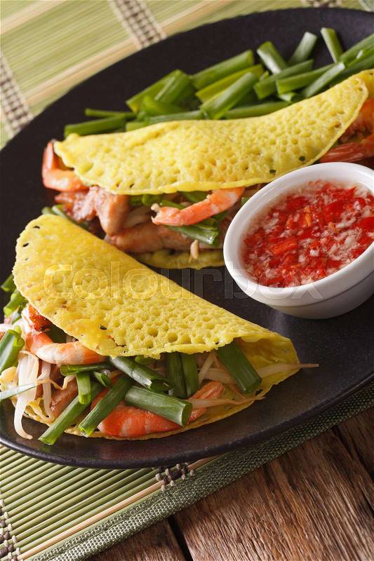 Vietnamese Banh Xeo crepes stuffed with pork, shrimp and bean sprouts and a spicy Nuoc Cham sauce closeup on a plate. Vertical\, stock photo