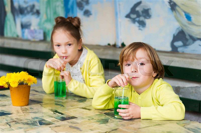 Two cute kids drinking green mint syrup in a cafe, stock photo