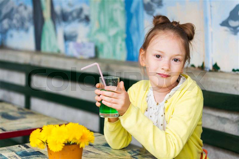 Adorable little girl drinking mint syrup in a cafe, wearing yellow jacket, stock photo