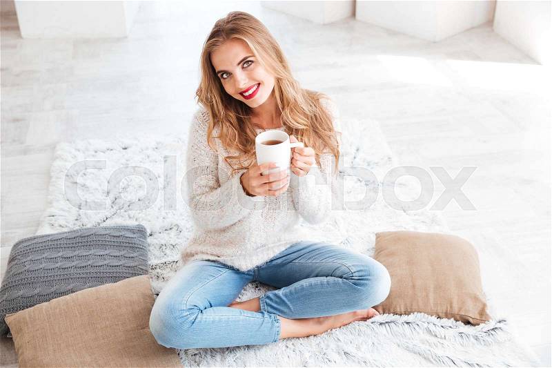 Close up portrait of a smiling happy girl in sweater holding tea cup indoors, stock photo
