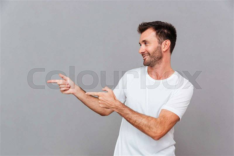 Portrait of a happy casual man pointing fingers away over grey background, stock photo