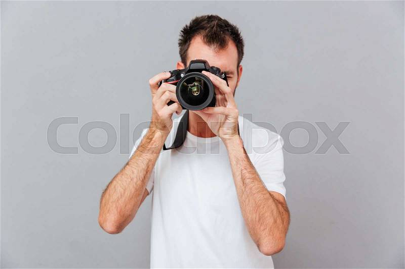 Portrait of a young photographer with camera isolated on a gray background, stock photo