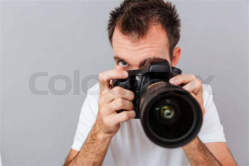 Portrait of a young photographer with camera isolated on a gray background, stock photo